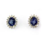 A pair of 18ct white gold (stamped 750) cluster earrings set with an oval cut sapphire surrounded by