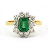 An 18ct yellow and white gold cluster ring set with a rub over set emerald cut emerald surrounded by