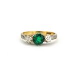 An 18ct yellow gold ring set with a round cut emerald flanked by brilliant cut diamonds, (M).