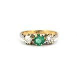An 18ct yellow and white gold ring set with a round cut emerald flanked by brilliant cut diamonds,