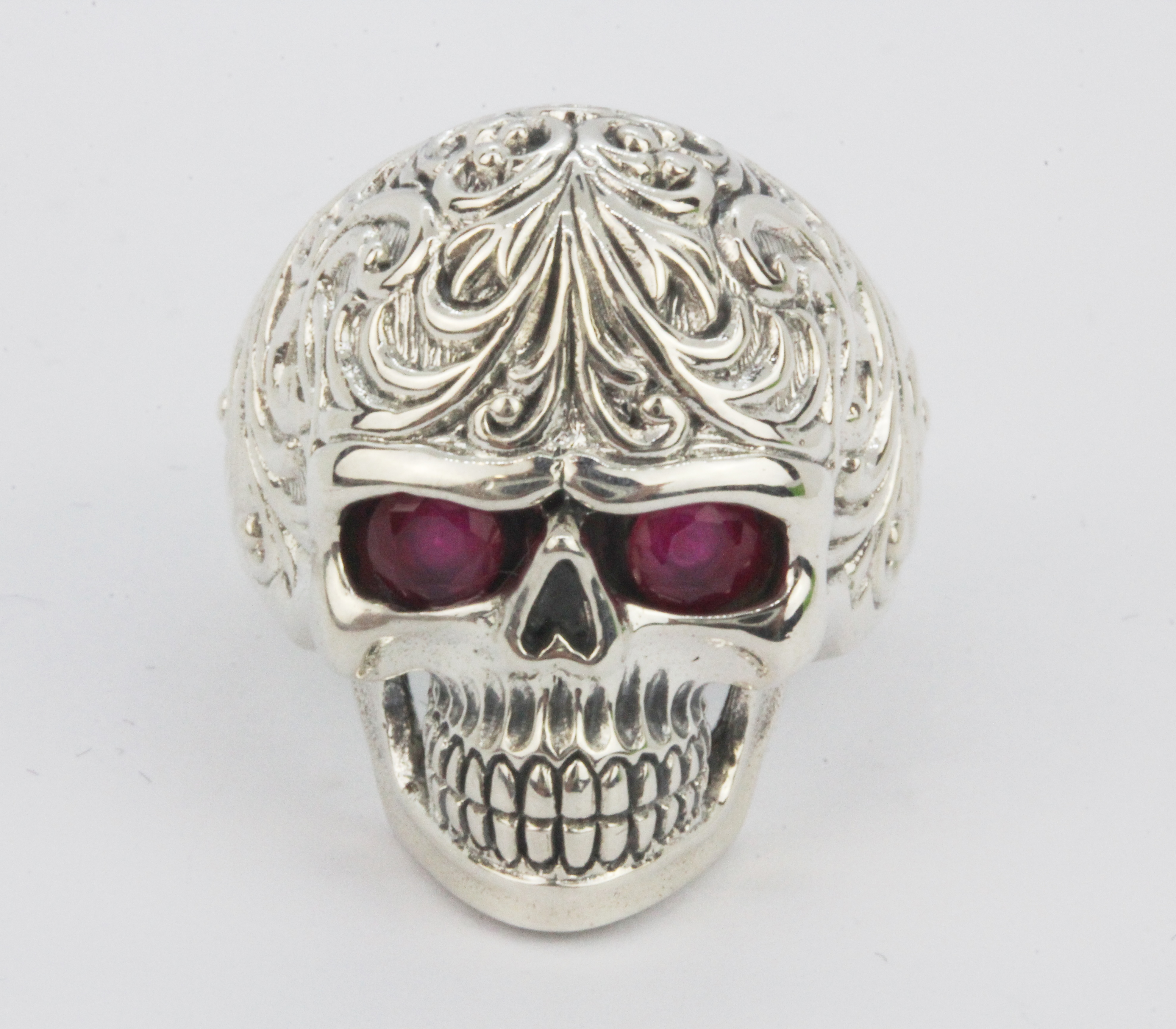 A 925 silver skull shaped ring with oval cut ruby set eyes, (R).