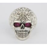 A 925 silver skull shaped ring with oval cut ruby set eyes, (R).