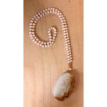 A Chinese carved mutton fat and russet jade dragon amulet on a strand of polished white jade