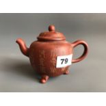 A small Yixing terracotta teapot raised on three feet and with slightly raised character decoration.