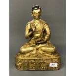 A large Tibetan gilt bronze figure of a seated Lama in meditation pose holding a book of teachings