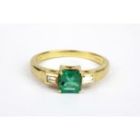 An 18ct yellow gold ring set with an emerald cut emerald and baguette cut diamond set shoulders, (