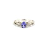 A 9ct white gold ring set with an oval cut tanzanite and diamond set shoulders, (L.5).