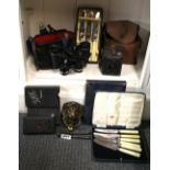 A mixed group of items including cameras, cutlery and binoculars.