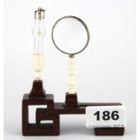 A carved 'grain of rice' ivory miniature with wooden stand and magnifying glass.