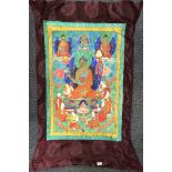 A Tibetan silk mounted hand painted of the seated golden Buddha with two further Buddhas above and