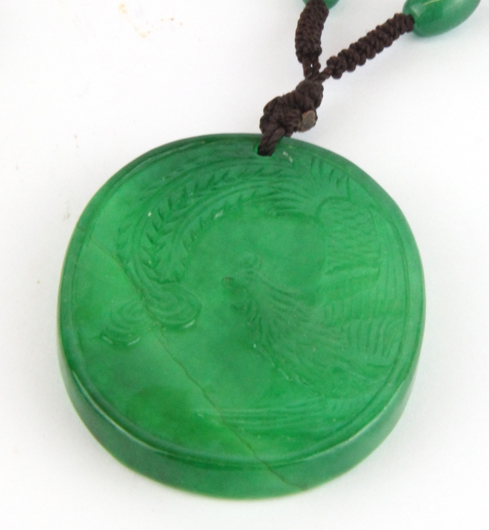 A Chinese carved green jade amulet of a phoenix on one side and a dragon on the other on a green - Image 2 of 2