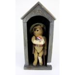 An early 20th Century hump back teddy bear in a WW1 uniform with button eyes, in a wooden sentry box