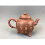 A small Yixing terracotta teapot raised on three feet and with slightly raised character decoration.
