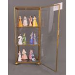 A small brass and glass display case containing a collection of twelve miniature porcelain lady