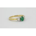 An 18ct yellow and white gold ring set with an oval cut emerald flanked by brilliant cut