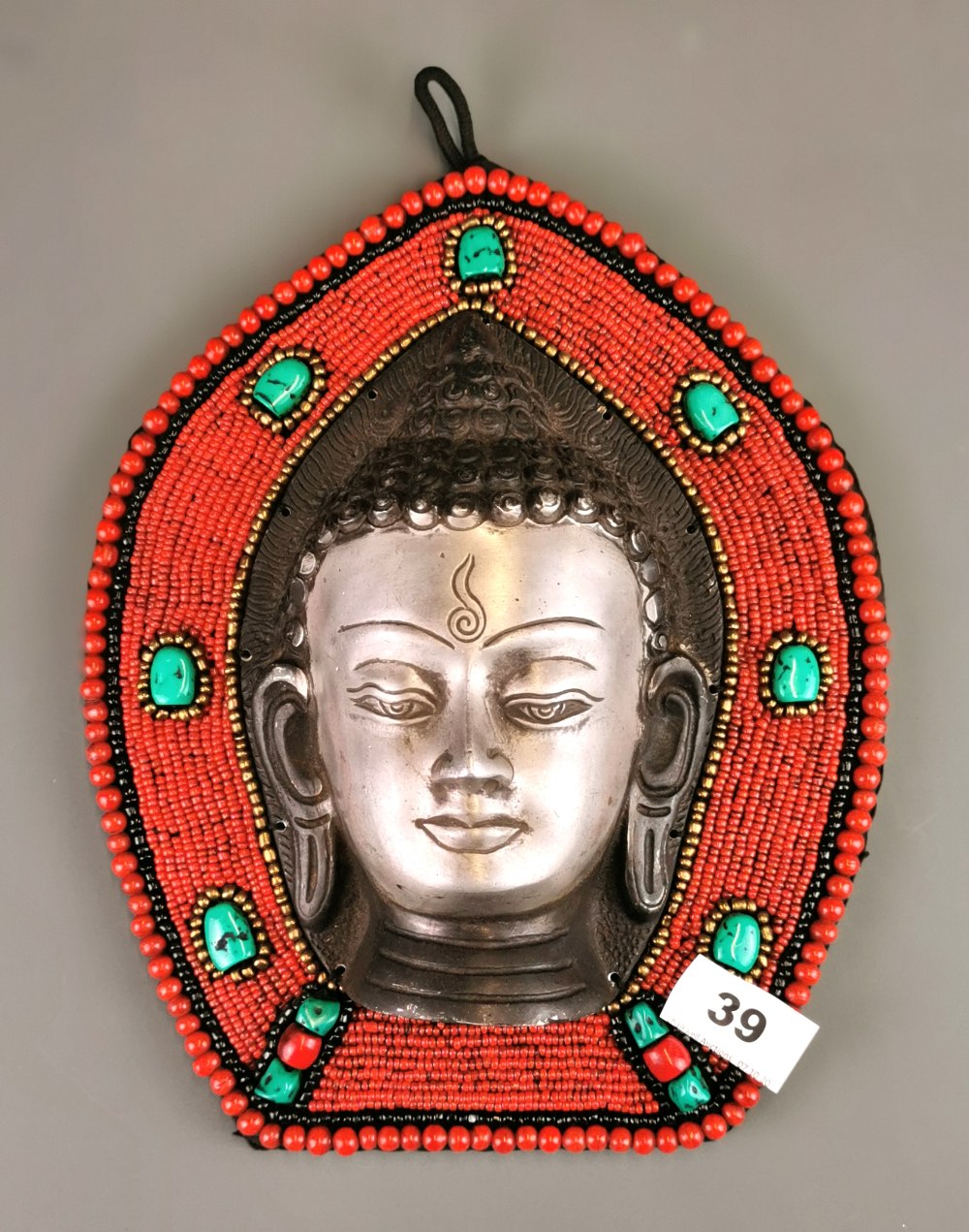 A Tibetan polished cast iron and bead mounted Buddha head wall panel, H. 28cm.