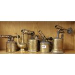 A group of four vintage brass blow torches and a brass jug.