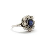 A white metal (tested platinum) cluster ring set with an oval cut sapphire surrounded by old cut