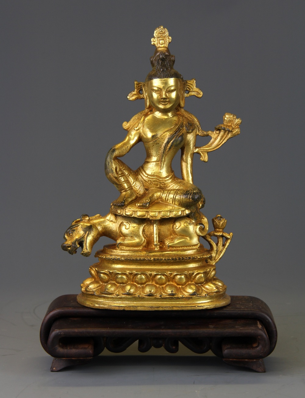 A Tibetan gilt bronze figure of a seated deity with an interlocking carved wooden stand.