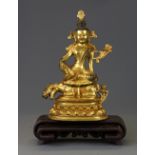 A Tibetan gilt bronze figure of a seated deity with an interlocking carved wooden stand.