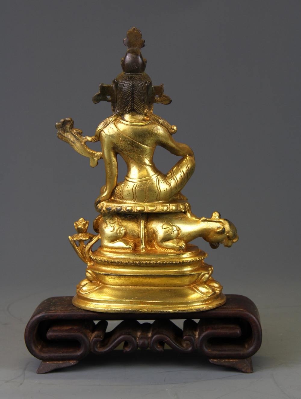 A Tibetan gilt bronze figure of a seated deity with an interlocking carved wooden stand. - Bild 2 aus 2