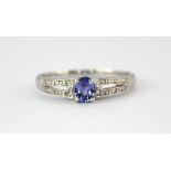 A 9ct white gold ring set with an oval cut tanzanite and diamond set shoulders, (P).