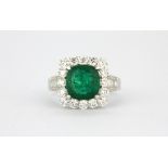 An 18ct white gold (stamped 750) ring set with a 3.65ct cushion cut emerald surrounded by