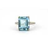 A white metal (tested high carat gold) ring set with an emerald cut aquamarine and brilliant cut