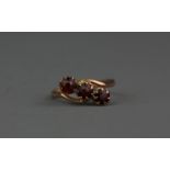 A 9ct yellow gold garnet set crossover ring, (J).