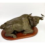 A Chinese bronze coloured terracotta figure of a water buffalo on a wooden pedestal, L. 46cm.
