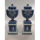 A pair of Adams blue and white jasperware pedestal urns and covers, sprigged with classical figures,