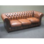 A modern Chesterfield three seater sofa, with button backed brown leather upholstery and three loose