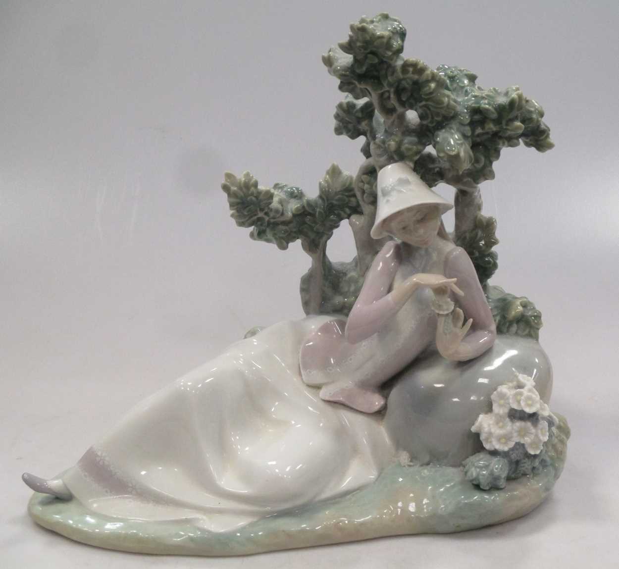 A Lladro figure of a lady reclining besides a tree