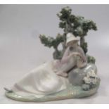 A Lladro figure of a lady reclining besides a tree