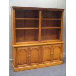 A modern oak bookcase with open shelves above cupboards, enclosed by two pairs of panelled doors,