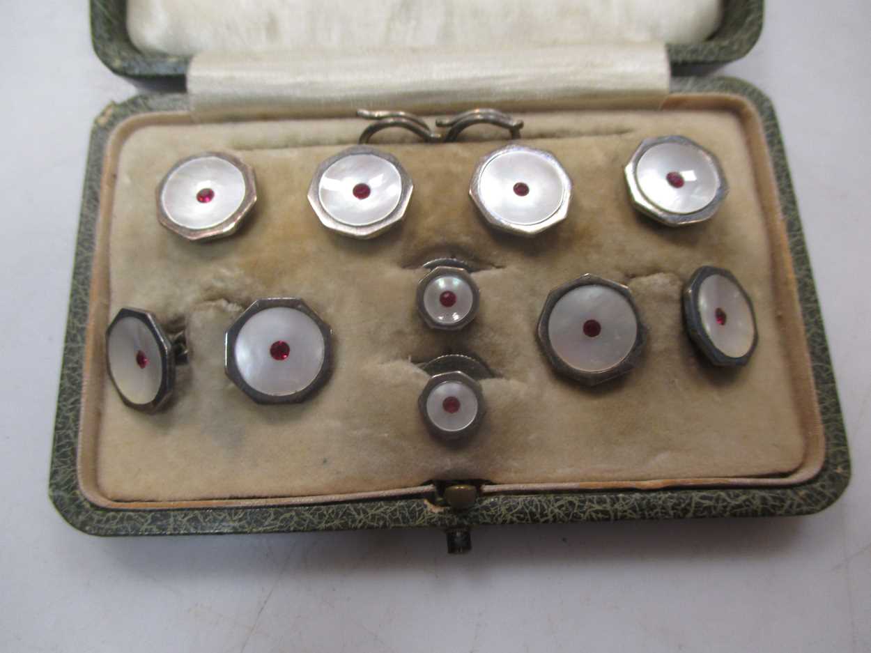 A cased gentleman's dress set, stamped 'silver' with mother of pearl and red paste decoration