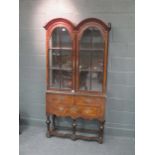 A Queen Anne style walnut cabinet on stand, with double domed top above two glazed doors