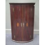 An early 19th century mahogany bow front corner cupboard with shell inlaid doors 111 x 68cm