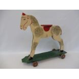 An early child's painted wooden ride-on horse on wheels.