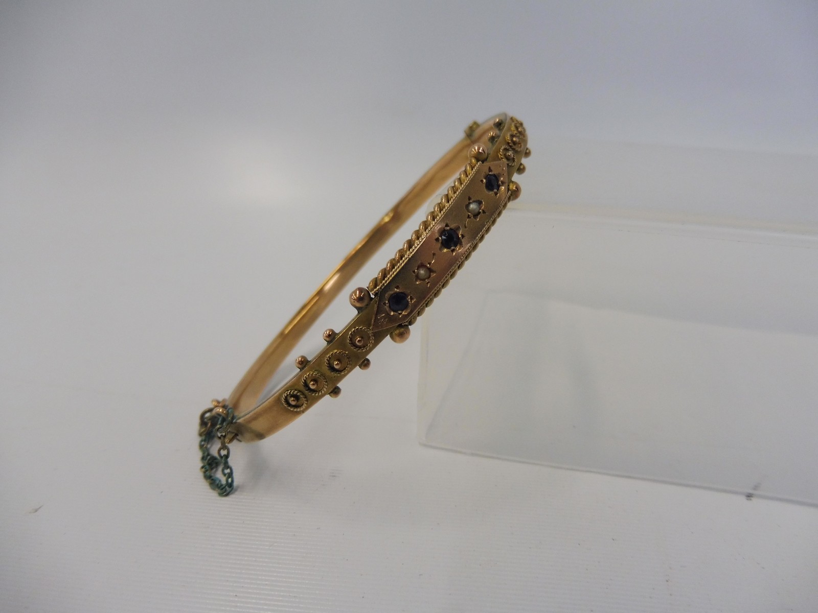 A 9ct gold bangle inset with sapphires and a seed pearl, weight approx. 8g.