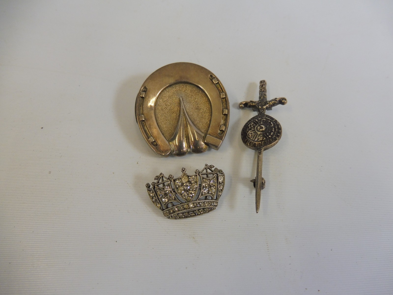 A silver horseshoe shaped brooch,a silver sword and shield brooch and one other