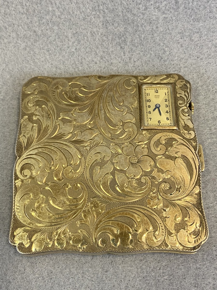 A silver compact case, with chased acanthus decoration and unusually inset with a watch movement