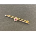 A yellow metal bar brooch set with a central stone (probably a ruby) surrounded by a ring of ten
