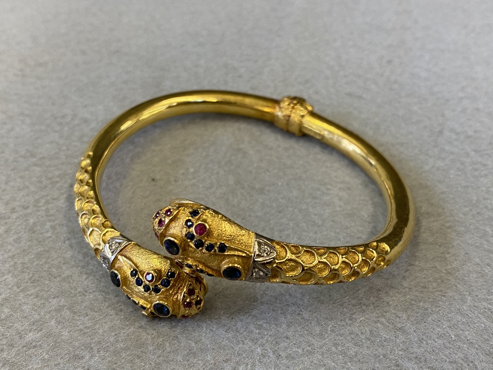 An 18k gold double headed serpent bangle, both heads encrusted with diamonds and semi-precious