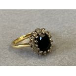 A 9ct gold ring set with a central stone of pale green/blue colour surrounded by a ring of
