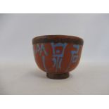 An unusual Chinese terracotta tea bowl with blue writing to the side.