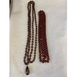 A long string of ruby coloured beads probably cherry amber, approximately 27" long and one similar