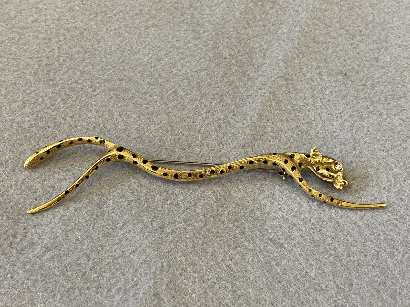 An 18ct gold brooch in the form of a cheetah with black enamel spots and a diamond inset forming the