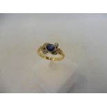 A yellow metal ring inset with a central sapphire and diamonds, in a Bravingtons leather and