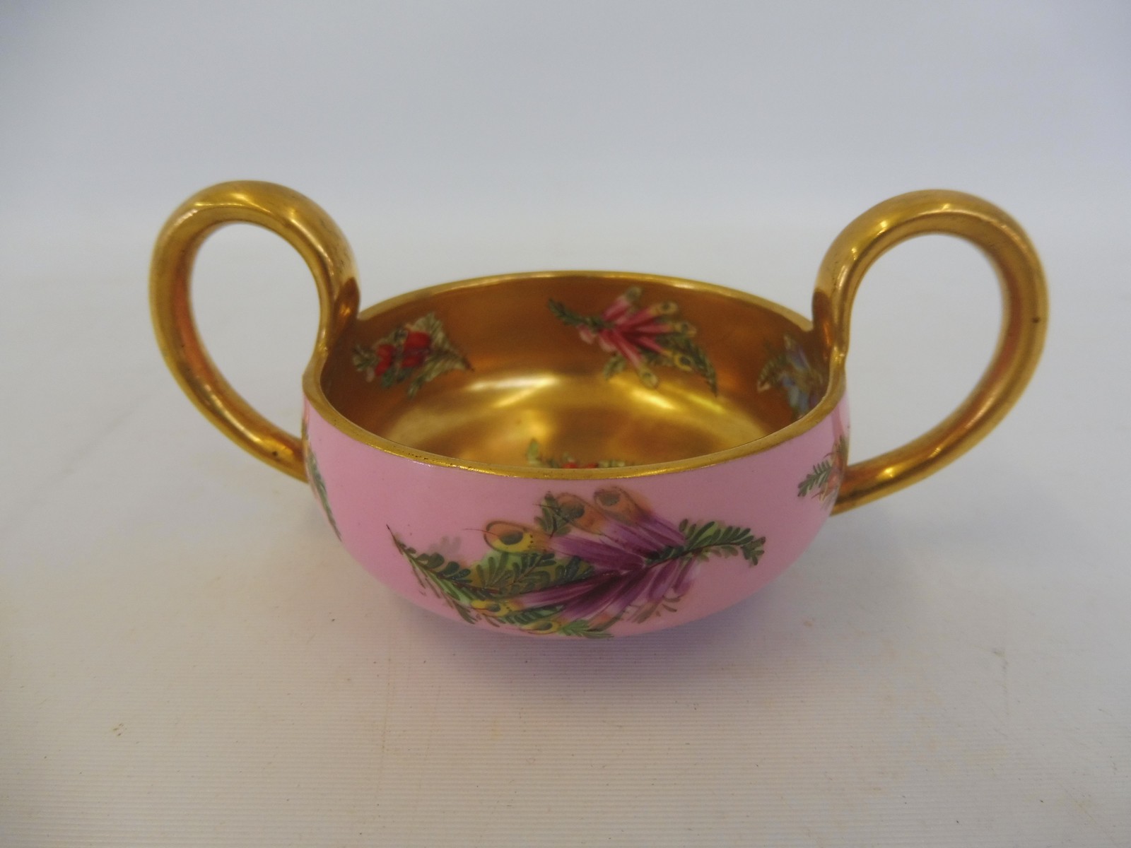 A Coalport porcelain two handled cup with gilded decoration and painted floral sprigs.